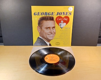 May include: A yellow vinyl record album cover featuring a portrait of George Jones with the title "Love Bug" and a list of songs including "Take Me", "Talk Back Trembling Lips", "Six Days On The Road", "The Bridge Washed Out", "Don't Let Me Cross Over", "Things Have Gone To Pieces", "My Friends Are Going To Be Strangers", "King Of The Road", "Don't Be Angry".