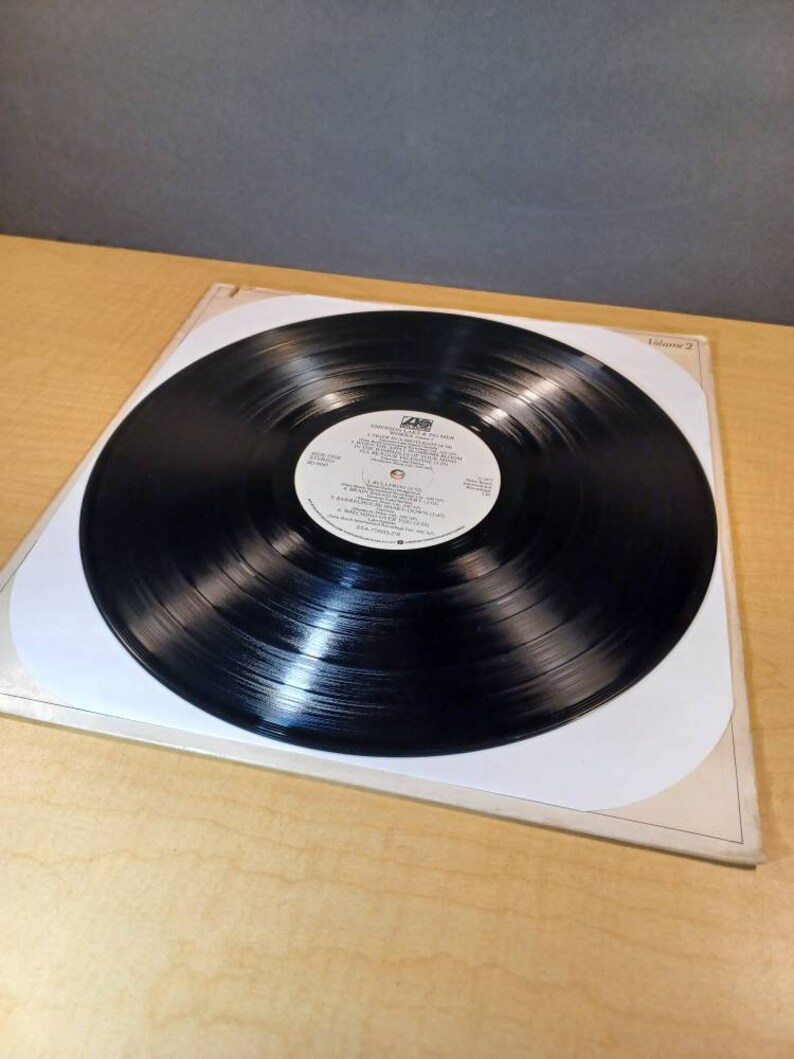 Puede incluir: Disco de vinilo negro con una etiqueta blanca. La etiqueta tiene el texto "SANDALWOOD" y "VOLUME 2" impreso en ella. El disco est&aacute; en una funda interior de papel blanco.