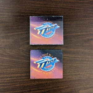 May include: Two compact disc cases with a blue and white logo of "The  707 Six Pack" on a brown wooden surface. The top case has the text "8 Classic Albums" and the bottom case has the text "A Taste Of..."