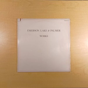 Puede incluir: Un &aacute;lbum de vinilo blanco con el texto "Emerson Lake & Palmer" y "Works" impreso en marr&oacute;n en la portada. El texto "Volumen 2" est&aacute; impreso en marr&oacute;n en la esquina superior derecha.