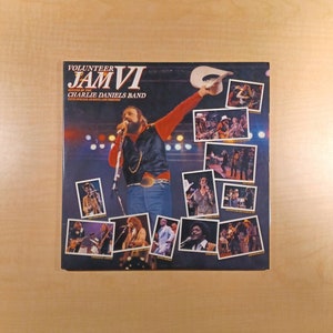 May include: A vinyl record album cover featuring Charlie Daniels Band's "Volunteer Jam VI" with special guests and friends. The cover features a collage of photos of the band members and guests performing on stage.