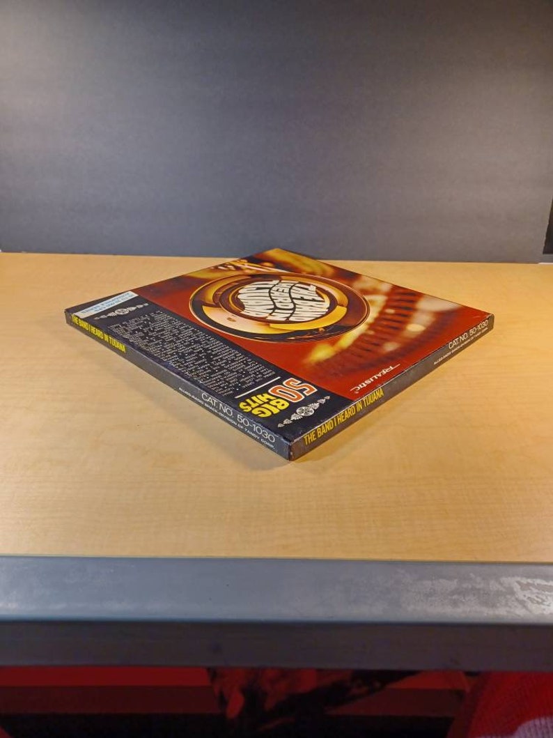 May include: A black and red record album cover with the text "50 Big Hits" and "The Band Heard In Tijuana" in white. The album cover features a gold trumpet with a red and white design.