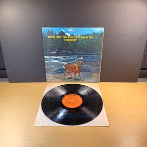 May include: A vinyl record album cover with a photo of a deer standing in a river. The album title is "Potter County Was Made By The Hand Of God" and the album artist is "Potter County Drifters".