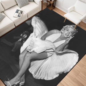 Puede incluir: Alfombra en blanco y negro con una imagen clásica de Marilyn Monroe con un vestido blanco. La alfombra muestra una fotografía vintage de la actriz, con un enfoque en su pose icónica y su vestido fluido. La alfombra es rectangular y adecuada para salones.