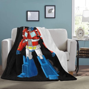 Puede incluir: Una manta de tiro negra y blanca con un robot de dibujos animados rojo, azul y blanco. El robot está de pie en una pose heroica con los brazos extendidos.