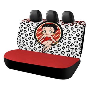 May include: Car seat cover featuring a red and black design with a Betty Boop graphic. The seat back has a white background with black leopard spots. The seat bottom is red, and the edges are black.