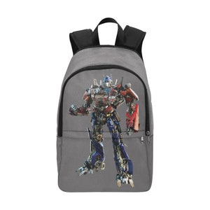 May include: A gray canvas backpack with a large image of Optimus Prime, a robot from the Transformers franchise, printed on the front. The robot is red, blue, and silver.