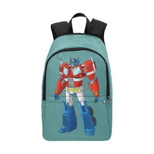 May include: A teal blue backpack with a large image of Optimus Prime, a red and blue robot from the Transformers franchise. The robot is standing in a heroic pose.
