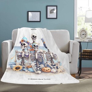 May include: White Halloween-themed blanket featuring a watercolor illustration of skeletons on a beach. The skeletons are adorned with floral crowns and scarves, with pumpkins and seashells. The blanket has the text "Halloween" and "ar aloveen dar as Turmer".