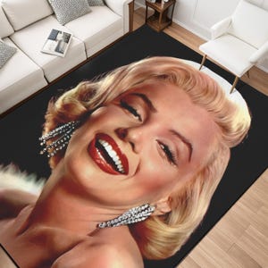 May include: A black rectangular area rug featuring a smiling portrait of a blonde woman with red lipstick and sparkling earrings. The rug is placed in a living room setting with white furniture and a wooden side table.