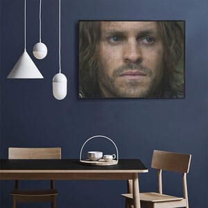 Op de afbeelding: Een close-up portret van een man met lang bruin haar en een baard. Hij kijkt recht in de camera met een serieuze uitdrukking. De afbeelding is in zwart-wit.