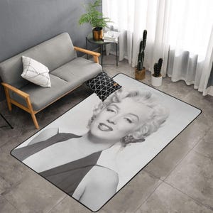 Puede incluir: Alfombra rectangular con una imagen en blanco y negro de Marilyn Monroe. La alfombra tiene un borde negro y está colocada sobre un suelo embaldosado. La imagen muestra a Monroe con su peinado característico y lápiz labial rojo.