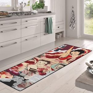 May include: A red, white, and black kitchen runner rug with a cartoon image of a woman in a red dress and cherries. The rug has a collage-style design with newspaper clippings and other images.