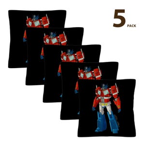 Puede incluir: Cinco cojines cuadrados negros con una ilustración roja, blanca, azul y plateada de Optimus Prime. El texto "5 PACK" está en la esquina superior derecha. Para decoración.