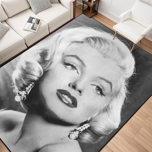 Puede incluir: Alfombra en blanco y negro con un primer plano del rostro de Marilyn Monroe. La alfombra muestra su icónico peinado, maquillaje y pendientes de perlas. La alfombra es rectangular y está colocada sobre un suelo de madera.