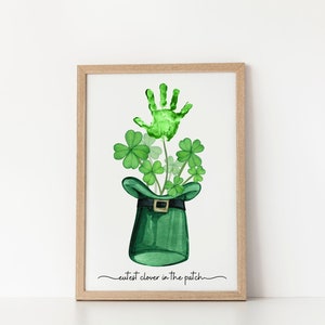 May include: A green handprint in the shape of a four-leaf clover, surrounded by other green clover leaves, inside a green leprechaun hat with a gold buckle. The text "cutest clover in the patch" is written below the hat.