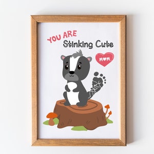 May include: A framed print with a cute cartoon skunk standing on a tree stump. The skunk has a black and white striped tail and a pink heart with the word "MOM" on it. The text "You are Stinking Cute" is written above the skunk.