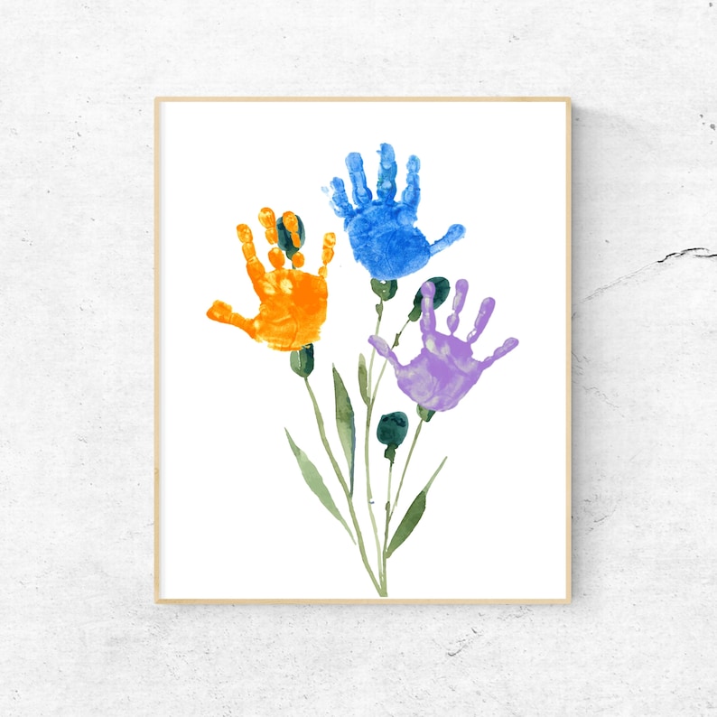 Puede incluir: Una impresi&oacute;n enmarcada de una obra de arte hecha con huellas de manos que representan tres flores. Las flores son azules, naranjas y moradas. Las huellas de manos est&aacute;n rodeadas de tallos y hojas verdes.
