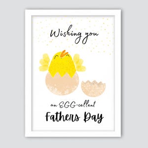May include: A framed print with a white border featuring a yellow chick hatching from an egg. The text reads "Wishing you an EGG-cellent Fathers Day" in black script and block letters, with gold speckles.