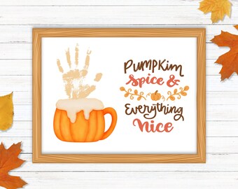 Può includere: Una stampa incorniciata con un'impronta di mano in vernice bianca su uno sfondo bianco. La stampa presenta un latte alla zucca e alle spezie con il testo "Pumpkin Spice & Everything Nice".