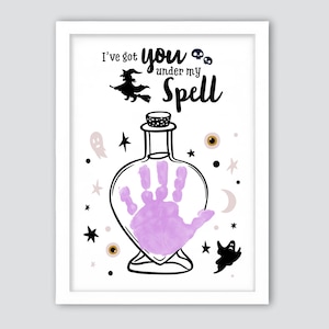May include: A framed Halloween-themed print with a white background. The print features a witch on a broom, a potion bottle with a purple handprint, and the text "I've got you under my Spell". Decorative elements include stars, ghosts, and eyeballs.