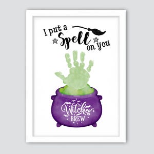 Puede incluir: Impresión enmarcada con temática de Halloween. La obra presenta una huella de mano verde sobre un caldero morado con la frase "Witches Brew". La frase "I put a Spell on you" está escrita encima de la huella, con un gráfico de escoba de bruja.