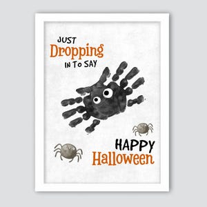 Puede incluir: Un estampado enmarcado con temática de Halloween con un diseño de araña de huella de mano. El estampado presenta el texto "JUST DROPPING IN TO SAY HAPPY Halloween" en naranja y negro. También se incluyen dos pequeñas arañas de dibujos animados.