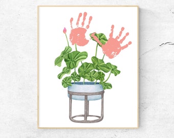 May include: Watercolor illustration of a potted plant with green leaves and pink handprints. The plant is in a light blue pot with a metal stand, set against a white background and framed in a light wood frame. A unique piece of art.