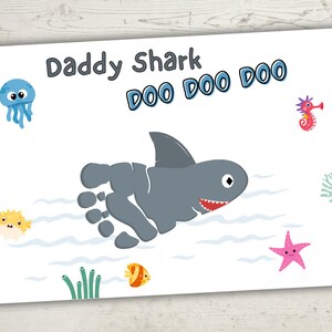May include: A white card with the text "Daddy Shark Doo Doo Doo" and a gray footprint shaped like a shark with a fin, teeth, and an eye. The card is decorated with a blue jellyfish, a pink starfish, a yellow pufferfish, a seahorse, and seaweed.