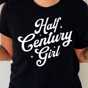 May include: Black t-shirt with white text that reads "Half Century Girl" with stars around the text.