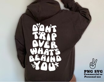 May include: A brown hoodie with a white graphic that says "Don't Trip Over What's Behind You". The graphic is in a retro, psychedelic font.