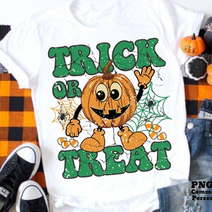 May include: White t-shirt with a green and orange graphic design. The graphic features a smiling pumpkin with the text "Trick or Treat" in a distressed font.