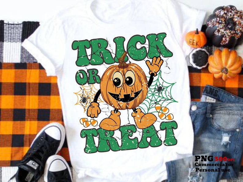 May include: White t-shirt with a green and orange graphic design. The graphic features a smiling pumpkin with the text "Trick or Treat" in a distressed font.