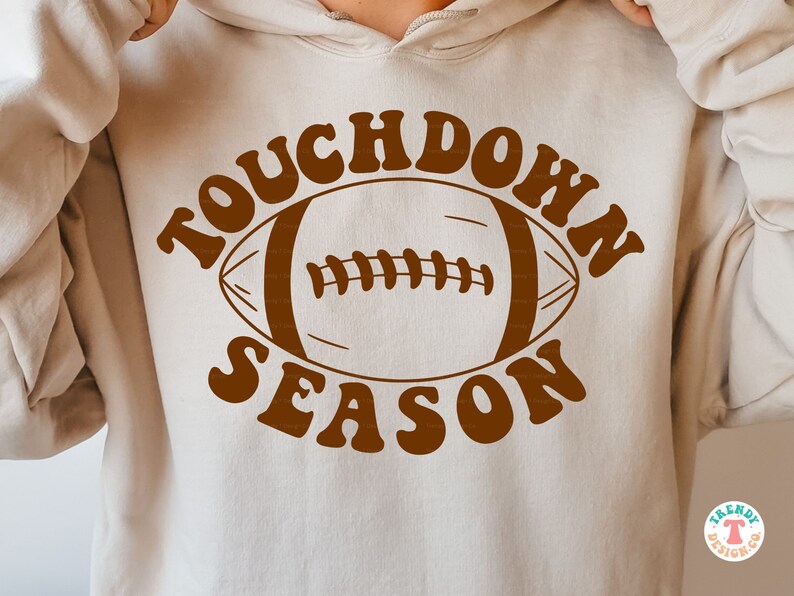 May include: A brown hoodie with the text "Touchdown Season" in a retro font. A brown football graphic is centered in the text.