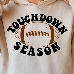 May include: A beige hoodie with the text "Touchdown Season" in black with a brown football graphic in the center.