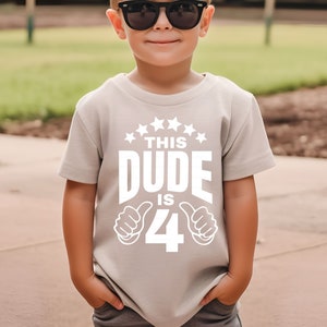May include: A light gray t-shirt with a white graphic that says "This Dude is 4" with thumbs up on either side of the number 4.