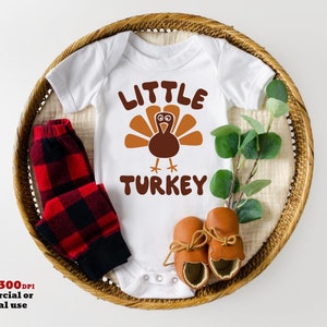 Puede incluir: Un body blanco para beb&eacute; con el texto "Little Turkey" y un dibujo de un pavo de dibujos animados. El body est&aacute; en una cesta de mimbre con una tela de cuadros rojos y negros y botines marrones.