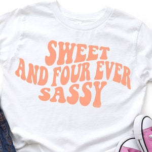 May include: White t-shirt with the text "Sweet and Four Ever Sassy" in pink, retro-style lettering.