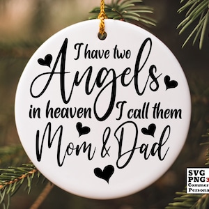 Può includere: Ornamento rotondo bianco con testo nero che recita "Ho due angeli in cielo che chiamo mamma e papà". Ci sono piccoli cuori neri intorno al testo.