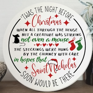 May include: White round sign with black text that reads "Twas the night before Christmas. When all through the house not a creature was stirring not even a mouse. The stockings were hung by the chimney with care in hopes that Saint Nicholas soon would be there."