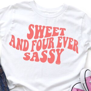 May include: White t-shirt with a pink graphic that says "Sweet and Four Ever Sassy" in a retro font.