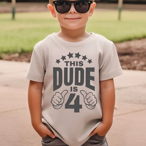 May include: A light gray t-shirt with a black graphic that says "This Dude is 4" with two thumbs up on either side of the number 4. The shirt has a row of five black stars above the text.