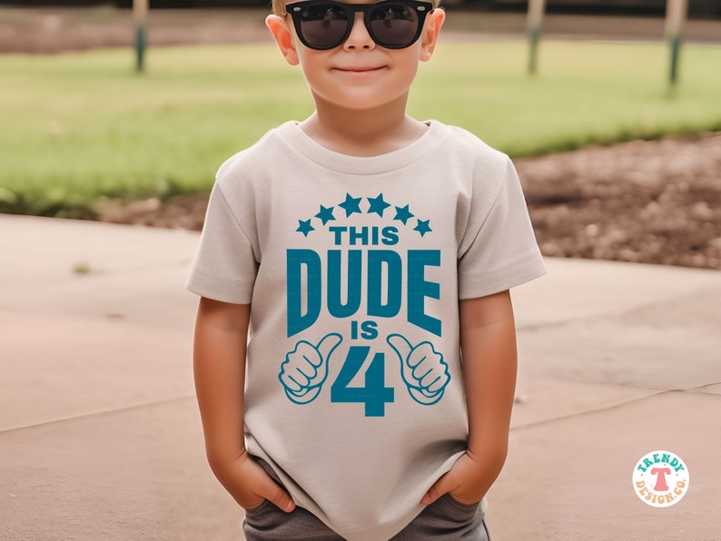 May include: A light gray t-shirt with a blue graphic that says "This Dude is 4" with thumbs up on either side of the number 4. There are five blue stars above the text.