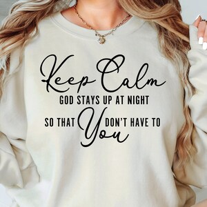May include: A beige sweatshirt with the text "Keep Calm God Stays Up At Night So That You Don't Have To" printed in black.