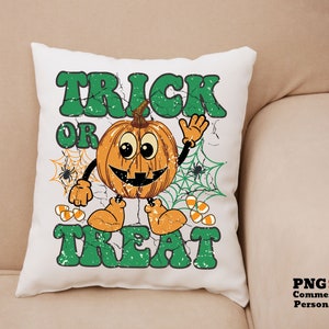May include: A white pillow with a green and orange Halloween design. The design features a smiling pumpkin with a spider web and the text "Trick or Treat".