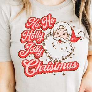 May include: A white t-shirt with a red and brown vintage-style graphic that says "Ho Ho Holly Jolly Christmas" and features a cartoon image of Santa Claus with a red hat.
