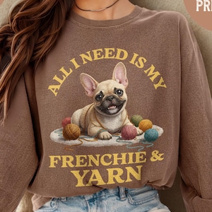 May include: Espresso-colored sweatshirt with a graphic of a French Bulldog surrounded by yarn balls. The text reads "ALL I NEED IS MY FRENCHIE & YARN." The sweatshirt is part of the Comfort Colors 6014 collection and is recommended to size up 1-2 sizes.