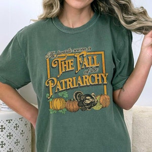May include: A green t-shirt with a vintage-style graphic that says "My favourite season is The Fall of the Patriarchy". The graphic features a turkey and pumpkins.