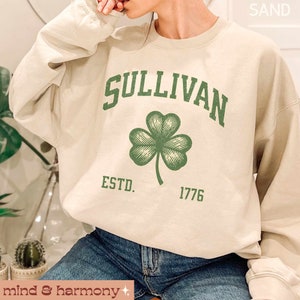 May include: A cream colored sweatshirt with the text "SULLIVAN ESTD. 1776" and a green shamrock graphic.