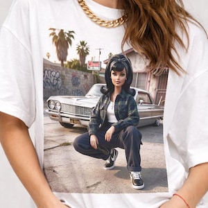 May include: White t-shirt featuring a graphic of a doll in a plaid shirt and dark pants, posing in front of a classic car. The shirt is worn with black shorts and a gold chain necklace.